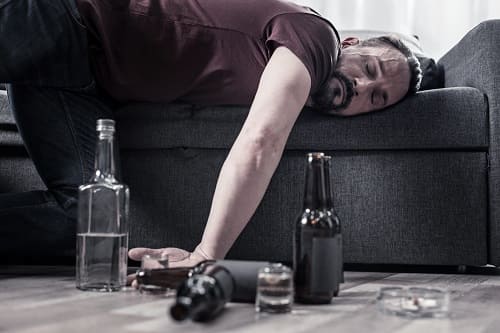 Мужчина лежит на диване рядом с бутылками